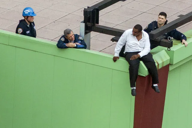 A man threatening suicide sits on a building ledge in New York's Times Square area, October 16, 2014. He was later persuaded and guided off the ledge safely by police. (Photo by Brendan McDermid/Reuters)