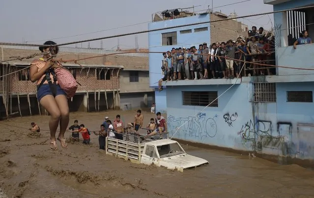 A woman is pulled to safety in a zipline harness in Lima, Peru, Friday, March 17, 2017. Intense rains and mudslides over the past three days have wrought havoc around the Andean nation and caught residents in Lima, a desert city of 10 million where it almost never rains, by surprise. (Photo by Martin Mejia/AP Photo)