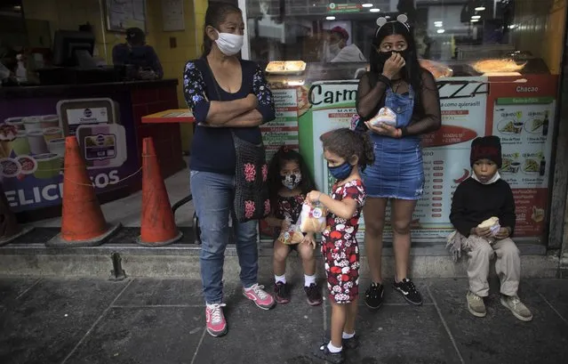 Residents, wearing protective face masks as a precaution against the spread of the new coronavirus, take shelter from the rain in Caracas, Venezuela, Tuesday, July 21, 2020. (Photo by Ariana Cubillos/AP Photo)