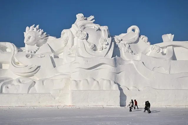 People walk next to a giant snow sculpture at the Harbin Sun Island International Snow Sculpture Art Expo in Harbin, in China's northeastern Heilongjiang province on January 4, 2023, ahead of the 39th Harbin China International Ice and Snow Festival. (Photo by Hector Retamal/AFP Photo)