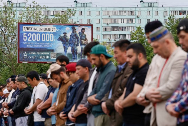 Muslims attend Eid al-Adha mass prayer, marking the end of the hajj pilgrimage, near a board promoting service in the Russian army and invites volunteers to sign a contract with the defence ministry, in Moscow, Russia on June 6, 2025. (Photo by Yulia Morozova/Reuters)