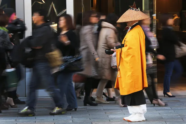 Shoppers walk past a Buddhist monk asking for alms in Tokyo's Ginza shopping district Tuesday, November 18, 2014. The news Monday that the economy contracted 1.6 percent in annual terms in July to September, following a 7.1 percent decline the previous quarter, virtually ensures that Japanese Prime Minister Shinzo Abe will decide Tuesday to delay a tax hike planned for October 2015. (Photo by Eugene Hoshiko/AP Photo)