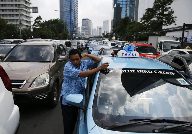 A taxi driver stands next to his vehicle as Indonesian workers block a road during a rally at the Bundaran Hotel Indonesia area in Jakarta December 10, 2014. Thousands of workers held the protest demanding the government to raise minimum wages after the government's decision to raise subsidized fuel price. (Photo by Reuters/Beawiharta)