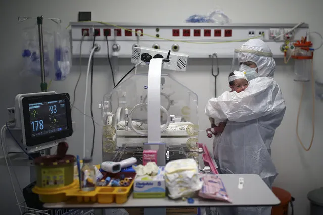 A nurse holds a 11-day-old baby boy infected with COVID-19, who arrived just four days after his birth at the intensive care unit of the Prof. Dr. Feriha Oz Emergency Hospital, after feeding him in Istanbul, Saturday, December 19, 2020. The hospital is a new infirmary offering some of the most advanced intensive care treatment in the country. When the pandemic first struck, Turkey was credited for quickly bringing infection rates under control. It is now seeing an explosion in COVID-19 cases that is putting a serious strain on its health system. (Photo by Emrah Gurel/AP Photo)