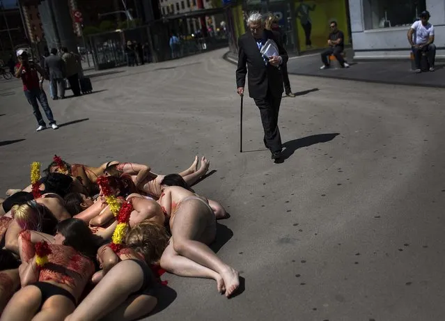 A man walks past partially clothed anti-bullfighting activists covered with fake blood as they pose for photographs during an event condemning bullfighting, in Barcelona, Spain, on May 23, 2013. (Photo by Emilio Morenatti/Associated Press)