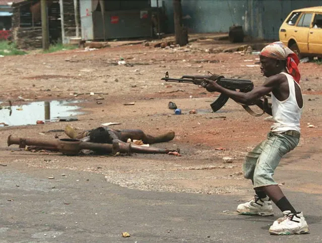 A boy, Kalashnikov in hand, leads a group of Charles Taylor's soldiers during heavy fighting around Monrovia's main military barracks, 16 April 1996 in Liberia. At least 15 corpses were scattered around. (Photo by Christophe Simon/AFP Photo)