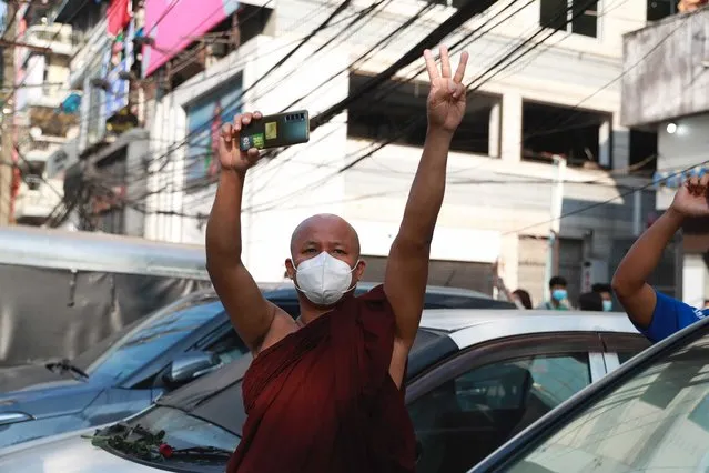 A Buddhist monk flashes the three-fingered salute as he watches protesters march in Yangon, Myanmar on Sunday, February 7, 2021. (Photo by AP Photo/Stringer)