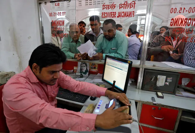 A cashier uses a machine to count 500 Indian rupee banknotes as customers wait in queues inside a post office in Lucknow, India, November 10, 2016. (Photo by Pawan Kumar/Reuters)