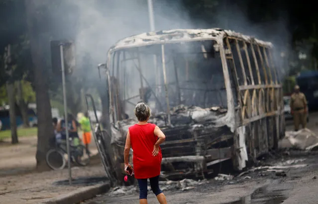 A woman looks at a burned bus near a protest against the Rio de Janeiro state government and a plan that will limit public spending in Rio de Janeiro, Brazil, November 16, 2016. (Photo by Ricardo Moraes/Reuters)