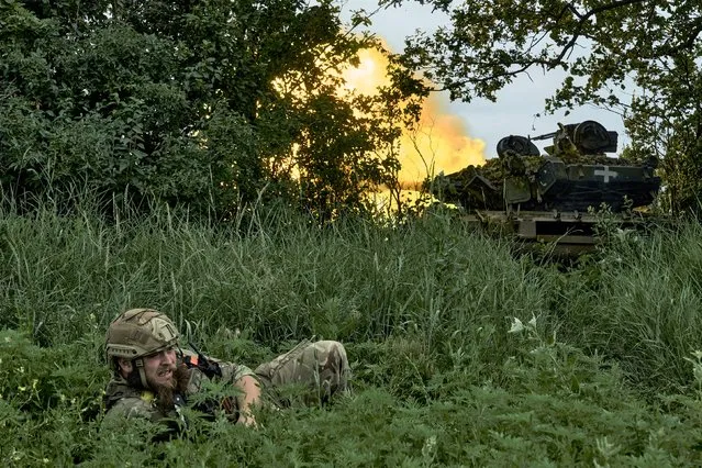 A Ukrainian soldier lies on the ground as a tank fires toward Russian positions at the frontline near Bakhmut, Donetsk region, Ukraine, Saturday, June 17, 2023. (Photo by Libkos/AP Photo)