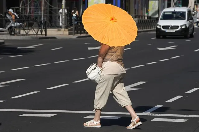 A woman crosses the street with a sun umbrella in Madrid, Spain, Saturday, June 24, 2023. Temperatures in Madrid rose to around 35 degrees centigrade Saturday with hotter weather expected in the coming days. (Photo by Paul White/AP Photo)