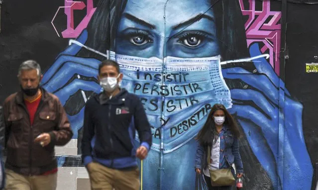 People wear face masks near a mural depicting a woman wearing a face mask in Bogota on April 14, 2021, amid the COVID-19 pandemic. Colombia announced the confinement of 12 million people against a third wave of covid-19. (Photo by Juan Barreto/AFP Photo)