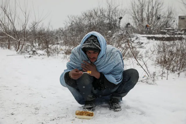 A migrant eats free food during a snowfall outside a derelict customs warehouse in Belgrade, Serbia January 9, 2017. (Photo by Marko Djurica/Reuters)