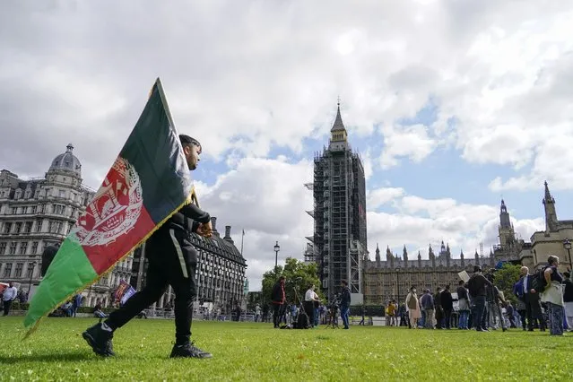 A demonstrator walks holding an Afghanistan flag, during a protest at Parliament Square in London, Wednesday, August 18, 2021. British Prime Minister Boris Johnson is set to update lawmakers Wednesday about the evacuation of British nationals and local allies from Afghanistan.  Big Ben's clock tower shrouded in scaffolding at centre. (Photo by Alberto Pezzali/AP Photo)