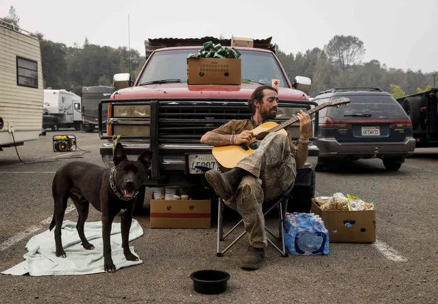 Grayson Howard plays the guitar while helping friends who evacuated to the the Green Valley Community Church evacuation shelter on Thursday, August 19, 2021, in Placerville, Calif., as the Caldor Fire continues to burn. (Photo by Ethan Swope/AP Photo)