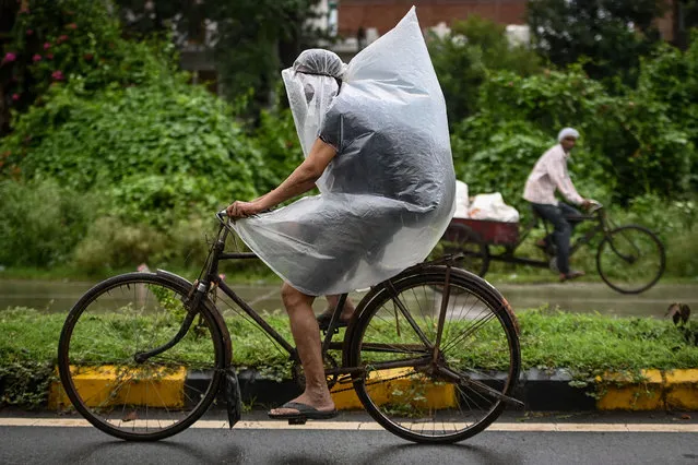 A cyclist covers himself with a plastic sheet during a downpour in Faridabad on September 1, 2021. (Photo by Money Sharma/AFP Photo)