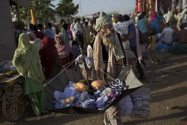 An Indian street vendor sells clothes in a makeshift camp for Sufi Muslim devotees during the Urs Festival in Ajmer, in the western Indian state of Rajasthan, India, Saturday, April 25, 2015. Thousands of pilgrims from different parts of India have arrived in the city for the yearly Urs that marks the death anniversary of the Sufi saint Khwaja Moinuddin Chishti. (Photo by Bernat Armangue/AP Photo)