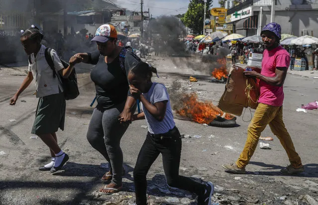 People walk past tires set fire as part of an anti-government protest in Port-au-Prince, Haiti, Thursday, October 21, 2021. (Photo by Joseph Odelyn/AP Photo)