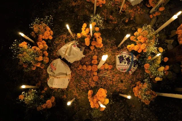 Flowers, food offerings and candles adorn a tomb as relatives spend the night next to the tomb of their loved one during Day of the Dead festivities at the the Arocutin cemetery in Michoacan state, Mexico, Monday, November 1, 2021. In a tradition that coincides with All Saints Day and All Souls Day, families decorate the graves of departed relatives with flowers and candles, and spend the night in the cemetery, eating and drinking as they keep company with their deceased loved ones. (Photo by Eduardo Verdugo/AP Photo)