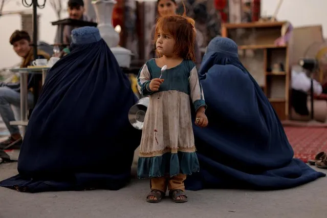 A girl stands between two women wearing burqas at a second hand market where people leaving the country sell their home appliances and other belongings, in Kabul, Afghanistan October 2, 2021. (Photo by Jorge Silva/Reuters)