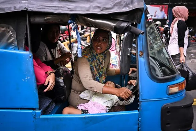 This picture taken on February 25, 2024 shows Bajaj driver and single mother Ekawati, who plies her three-wheeled taxi in a profession overwhelmingly dominated by men in Indonesia's capital city, transporting customers while her three-year-old daughter Debi rests on her lap while on their rounds in Jakarta. Her three-year-old perched in her lap, single mother Ekawati plies Jakarta's notorious traffic in her three-wheeled autorickshaw, making ends meet as one of a growing number of Indonesian women seeking informal employment outside the home. (Photo by Adek Berry/AFP Photo)