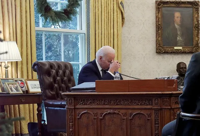 U.S. President Joe Biden is seen through a glass doorway as he speaks by phone with Ukraine's President Volodymyr Zelenskiy in the Oval Office at the White House in Washington, U.S., December 9, 2021. (Photo by Leah Millis/Reuters)