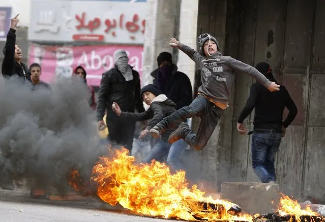 A Palestinian youth throws a stone towards Israeli soldiers as he jumps over burning tyres during clashes that followed a rally to support President Mahmoud Abbas in the West Bank city of Hebron March 17, 2014. Thousands of Palestinians took to the streets on Monday to show their support for Abbas, who is under heavy pressure as he prepares to meet U.S. President Barack Obama. (Photo by Mussa Qawasma/Reuters)