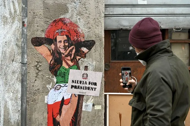 A man takes a photo of a mural entitled “Thank goodness Silvia is here” (Meno male che Silvia c'è), representing former Italian prime minister and presidential candidate Silvio Berlusconi dressed as a woman, by Italian street artist Salvatore Benintende aka TvBoy, on January 21, 2022 in Milan. (Photo by Piero Cruciatti/AFP Photo)