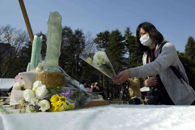 A visitor offers flower at a makeshift altar to mourn for the victims of the March 11, 2011 earthquake and tsunami during a special memorial event Friday, March 11, 2022, in Tokyo. Japan on Friday marked the 11th anniversary of the massive earthquake, tsunami and nuclear disaster that struck Japan's northeastern coast. (Photo by Eugene Hoshiko/AP Photo)