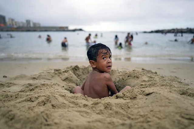 A little boy digs a hole in the sand at the beach during Carnival celebrations in La Guaira, Venezuela, Monday, Feb. 28, 2022. (Photo by Ariana Cubillos/AP Photo)