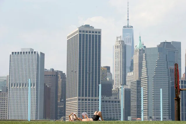 The skyline of lower Manhattan is seen as people lay on the grass in Brooklyn Bridge Park in the Brooklyn borough of New York City, U.S., May 27, 2016. (Photo by Brendan McDermid/Reuters)