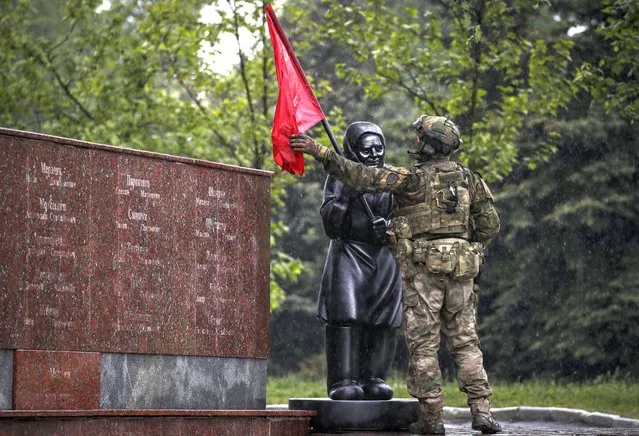 A picture taken during a visit to Mariupol organized by the Russian military shows a Russian serviceman adjusting the Soviet flag on a statue of a grandmother in Leninsky Komsomol Square in downtown of Mariupol, Ukraine, 18 May 2022. The statue was erected in early May and it relates to a video that started circulating in April showing an elderly woman in a village on the outskirts of Kharkiv waving the Soviet flag to Ukrainian troops, mistaken them for Russian soldiers. On 24 February, Russian troops invaded Ukrainian territory starting a conflict that has provoked destruction and a humanitarian crisis. According to the UNHCR, more than six million refugees have fled Ukraine, and a further 7.7 million people have been displaced internally within Ukraine since. (Photo by Sergei Ilnitsky/EPA/EFE)