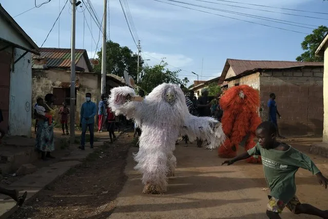 A boy runs away from men dressed as Kankurang during a ritual procession in Bakau, Gambia, Saturday, October 2, 2021. The Kankurang rite was recognized in 2005 by UNESCO, which proclaimed it a cultural heritage. Despite his fearsome appearance, the Kankurang symbolizes the spirit that provides order and justice and is considered a protector against evil. He appears at ceremonies where circumcised boys are taught cultural practices, including discipline and respect. (Photo by Leo Correa/AP Photo)