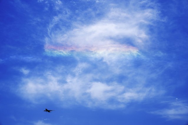 A passenger airliner flies past a rainbow on the clouds cast by the sunlight in the sky over the city in Beijing, Tuesday, May 14, 2024. (Photo by Andy Wong/AP Photo)