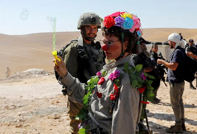 A peace activist dressed as a clown blows bubbles as Israeli machineries guarded by Israeli forces demolish a Palestinian house in Masafer Yatta, in the Israeli-occupied West Bank on July 4, 2022. (Photo by Mussa Qawasma/Reuters)