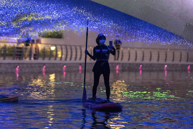 A woman wearing a mask takes a selfie as she paddles underneath a bridge with colourful lights along a canal, Friday, July 1, 2022, in Beijing. (Photo by Ng Han Guan/AP Photo)