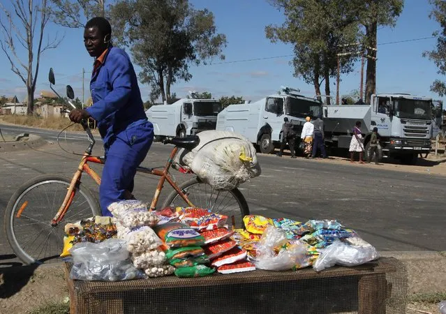 A cyclist buys a snack from a street trader as anti-riot police vehicles and water canons are seen in Epworth near Harare, Zimbabwe, July 5, 2016. (Photo by Philimon Bulawayo/Reuters)