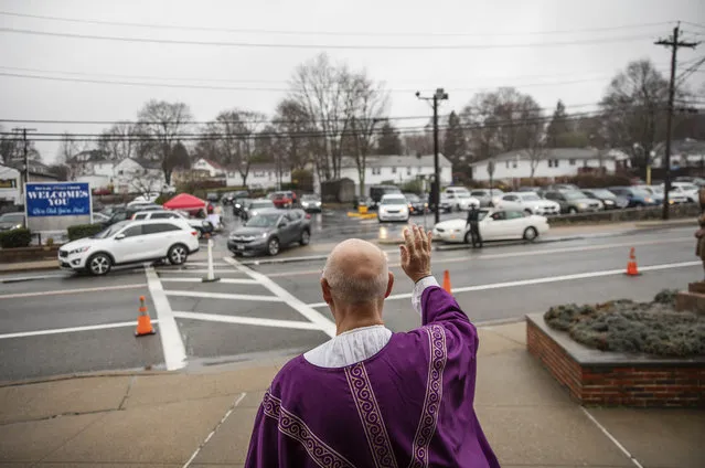 Rev. Peter Gower waves to worshippers as they leave the parking lot where they listened over their radios to Mass he held from the front door of Our Lady of Grace Catholic Church, Sunday, March 29, 2020, in Johnston, R.I. Gower started the Mass for those to attend from their cars last week as gatherings became restricted due to the coronavirus. (Photo by David Goldman/AP Photo)