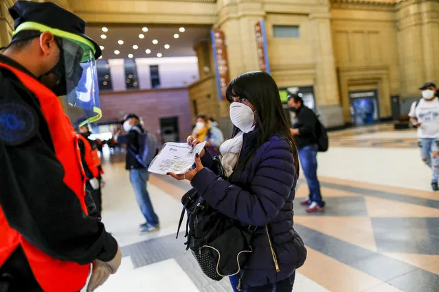 A woman wearing a face mask shows papers to a police officer at a checkpoint in Constitucion railway station, as the spread of the coronavirus disease (COVID-19) continues, in Buenos Aires, Argentina on April 16, 2020. (Photo by Agustin Marcarian/Reuters)