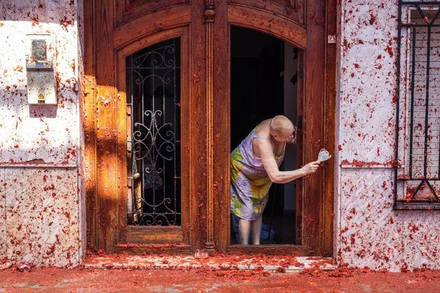 Carmen Sez (71), a resident of the village, cleans the tomato remains from the front door of her house after the Tomatina festival on August 31, 2022 in Bunol, Spain. The world's largest food fight festival, La Tomatina, consists of throwing overripe and low-quality tomatoes at each other. (Photo by Zowy Voeten/Getty Images)