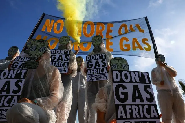 A climate activist from Extinction Rebellion holds a smoke flare while others carry placards outside the Africa Energy Week Conference as they staged a protest against the oil and gas industry, which they believe leads Africa down a path of environmental destruction, stranded assets, energy poverty and economic disaster, in Cape Town, South Africa on October 18, 2022. (Photo by Esa Alexander/Reuters)