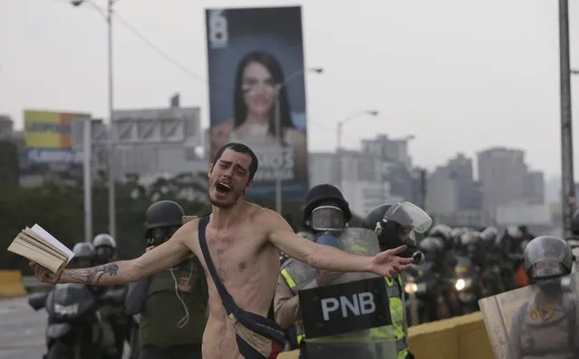 An anti-government protester holds a bible under the watch of riot police during a march against President Nicolas Maduro  in Caracas, Venezuela, Thursday, April 20, 2017. Tens of thousands of protesters flooded the streets again, one day after three people were killed and hundreds arrested in the biggest anti-government demonstrations in years. (Photo by Fernando Llano/AP Photo)