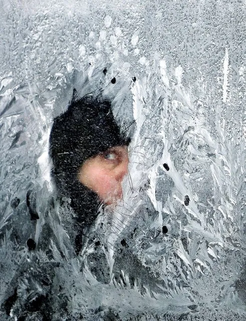 A woman peers out of a frost-covered bus window in Bucharest, Romania on February 1, 2012. (Photo by Vadim Ghirda/Associated Press)