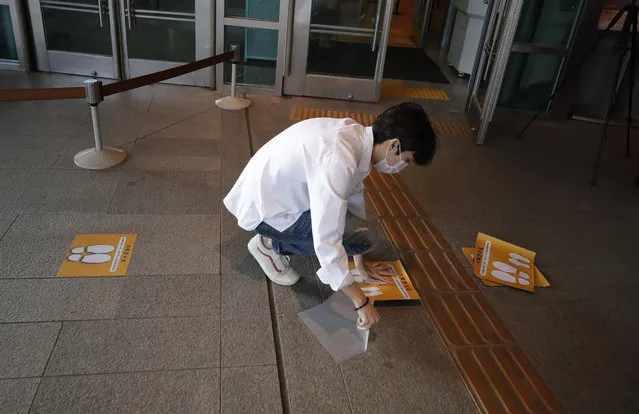 A man wearing a face mask attaches social distancing signs on the floor at the National Museum of Korea in Seoul, South Korea, Monday, September 28, 2020. The museum reopened Monday after having been closed for six weeks as a precaution against the coronavirus. (Photo by Lee Jin-man/AP Photo)