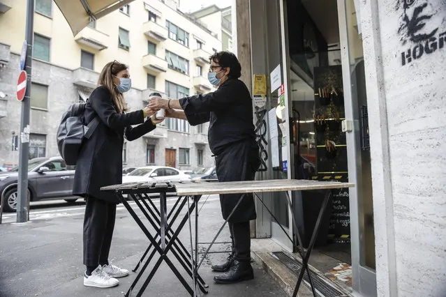 Bar owner Franco Epifani delivers cappuccino to a customer outside his bistrot bar, at Isola district, in Milan, Italy, Friday, November 6, 2020. Lombardy is among the four Italian regions classified as red zones, where a strict lockdown will be imposed and reassessed in two weeks to curb the infections growing curve. (Photo by Luca Bruno/AP Photo)