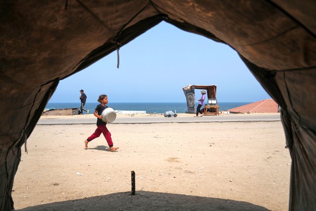 A Palestinian girl runs with an empty basin to a water distribution point during a hot summer day with temperatures reaching 36 °C (97 °F) in Deir al-Balah, in the central Gaza Strip, Wednesday, August 13, 2025. The youth behind her pulls containers of water. (Photo by Abdel Kareem Hana/AP Photo)