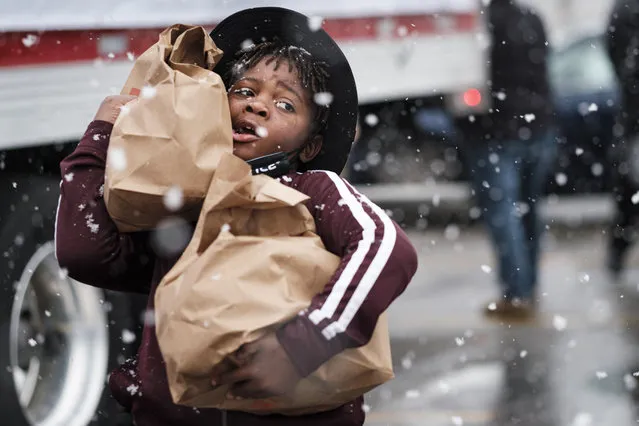 A child volunteering at a food distribution carries bags of food to people in line during a Thanksgiving food distribution at a park in Des Moines during a snowstorm on November 23, 2020. The food distribution was organized by Urban Dreams, a community empowerment NGO in central Des Moines, and the NAACP. The food was provided by Hy-Vee, a regional grocery store chain based in Des Moines. The Food Bank of Iowa said food insecurity in Des Moines has doubled since the start of the Coronavirus pandemic. (Photo by Jack Kurtz/ZUMA Wire/Rex Features/Shutterstock)