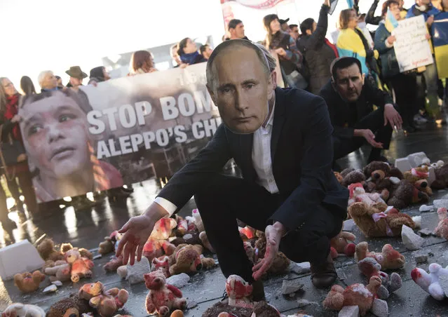 An activist wearing a mask depicting Russian President Vladimir Putin knees inmid colour smeared teddy bears during a protest on October 19, 2016 in front of the chancellery in Berlin ahead of a meeting of leaders of Russia, Ukraine, France and Germany. German Chancellor Angela Merkel hosts the leaders in a new push for peace in eastern Ukraine and for a “working meeting” afterwards on the war in Syria. (Photo by Steffi Loos/AFP Photo)