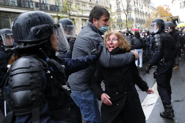 A riot police officer pushes a couple during a protest, Saturday, December 12, 2020 in Paris. (Photo by Thibault Camus/AP Photo)