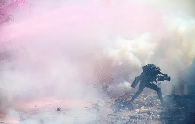A journalist runs through teargas lobbed by riot police officers to disperse the convoy of Kenya's opposition leader Raila Odinga of the Azimio La Umoja (Declaration of Unity) One Kenya Alliance, as they participate in a nationwide protest over cost of living and President William Ruto's government in Nairobi, Kenya on March 30, 2023. (Photo by Reuters/Stringer)